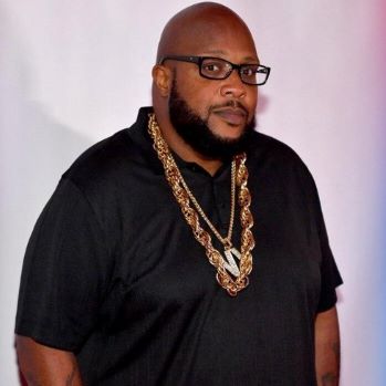 Bald African American man in black shirt wearing glasses and several gold necklaces