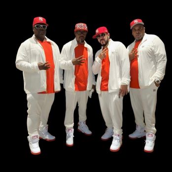 Four African American men wearing white suits, orange shirts, and matching orange baseball caps