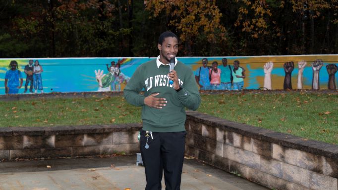 African American man with microphone wearing a green SUNY Old Westbury sweatshirt