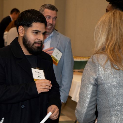 Hispanic male student with a beard holds conversation with woman with blonde hair