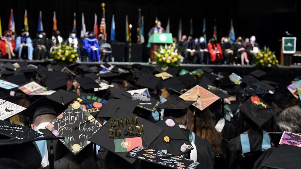 View from the audience of the overlooking approximately 50 graduates with decorated mortarboards