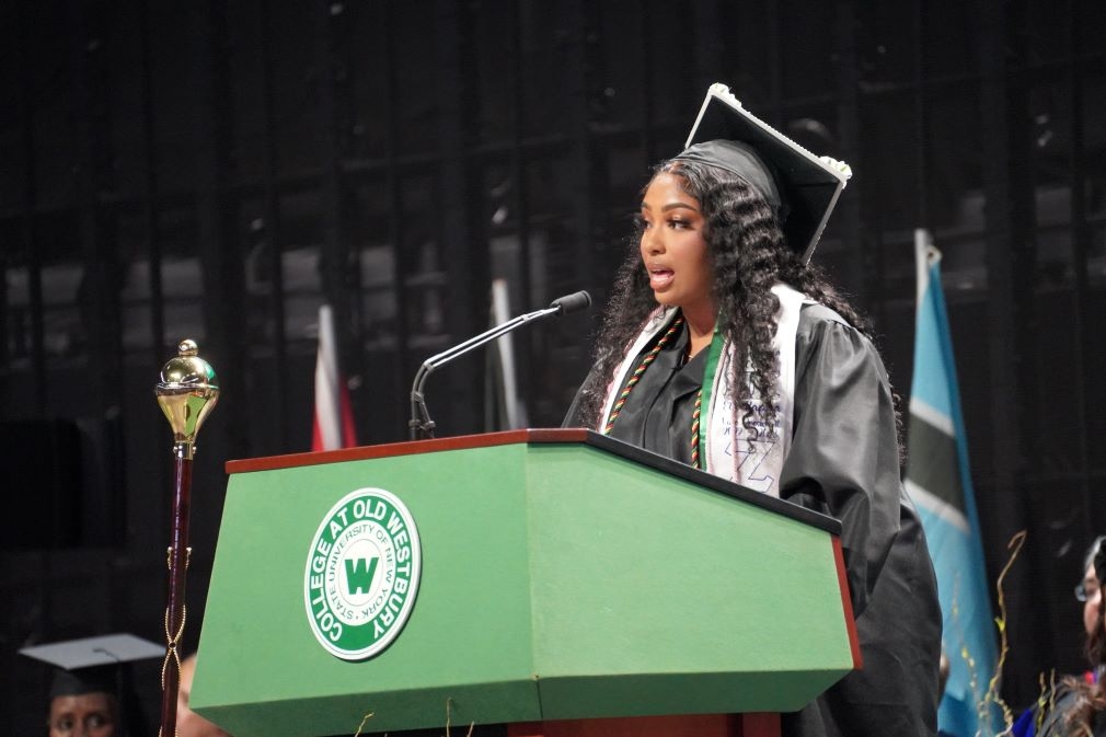 Kimberly Cox in cap and gown speaking at a podium