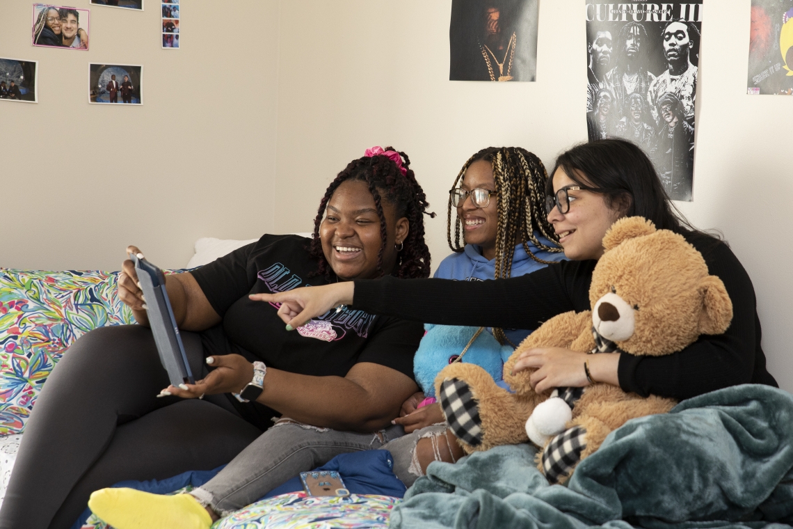 Three female students looking at a laptop while sitting in a residential room