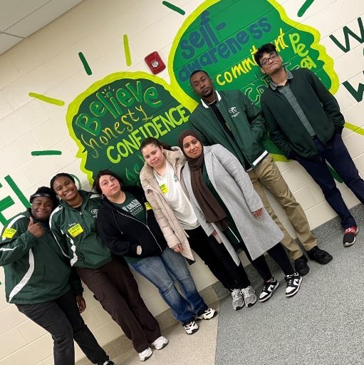 A group of students posing in front of a wall with green writing.