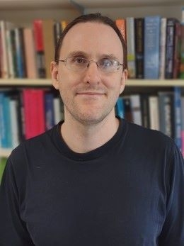 Dr. Estes with glasses in front of bookcase