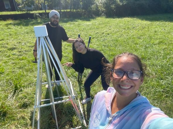 Three young people in a field with a radio astronomy antenna