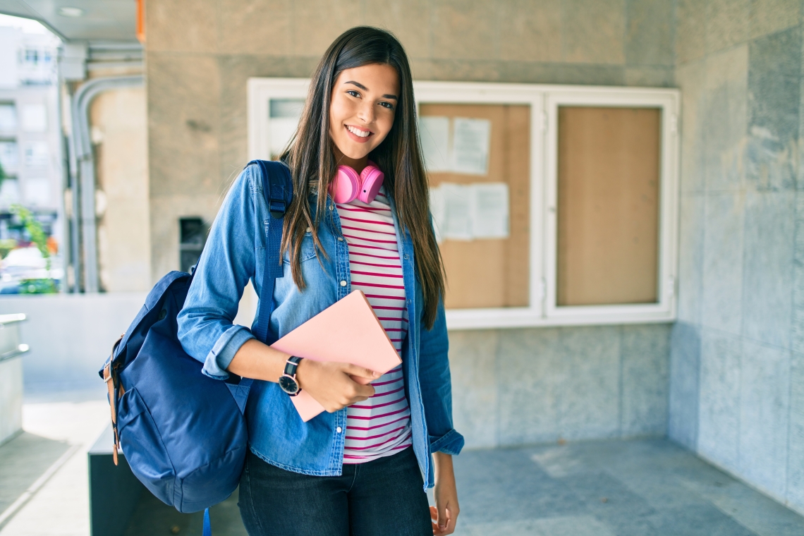 A female student with long straight hair carrying a book and a backpack