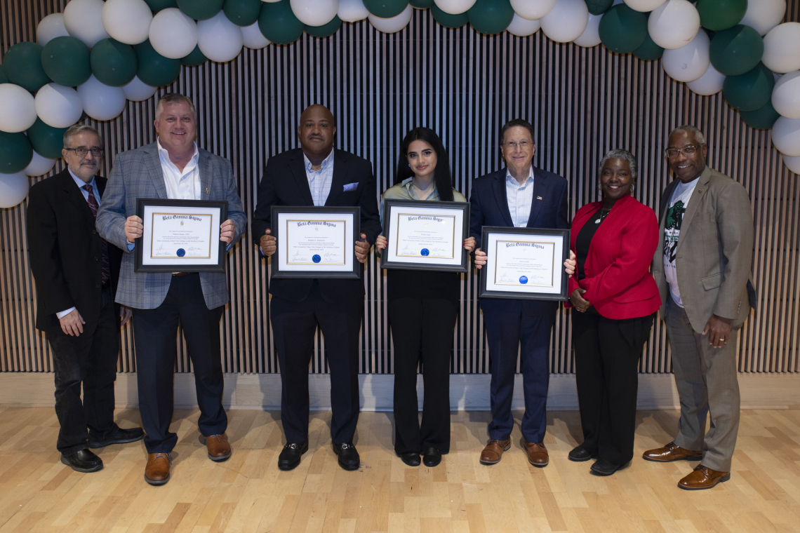 Four awardees holding certificates are congratulated by three campus officials