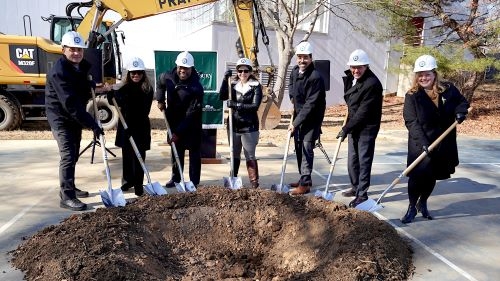 Seven people wearing hard hats and holding shovels