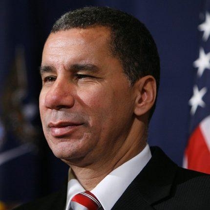 African American man in suit with American flag behind him