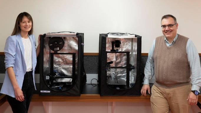 Two professors pose alongside two 3D printers