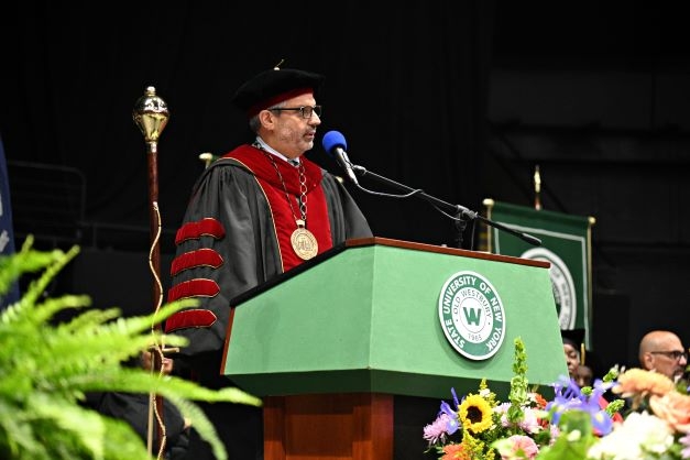 A Hispanic man in red regalia behind a podium