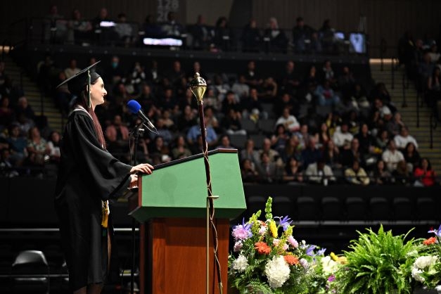 A white woman in black regalia speaks before a large crowd