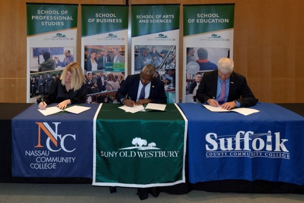 Three college presidents seated at table signing documents