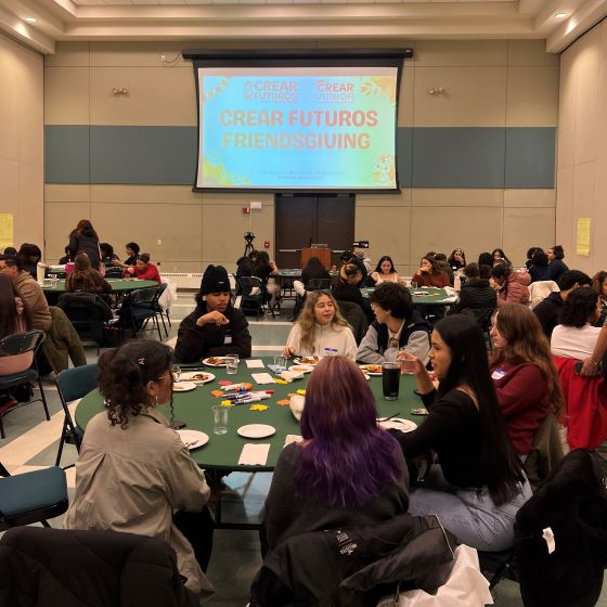 Room full of students at tables with a large sign reading "Friendsgiving"