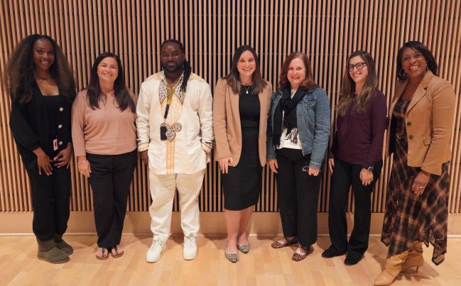 Group photo of seven diverse people posing on stage
