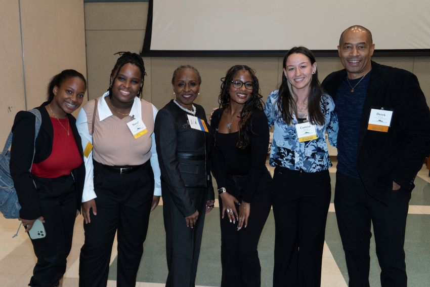Five women and one man, all in business casual attire, pose for a group photo