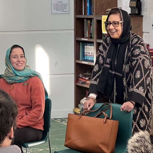 One white woman and one middle Eastern women wearing hijabs and holding a conversation