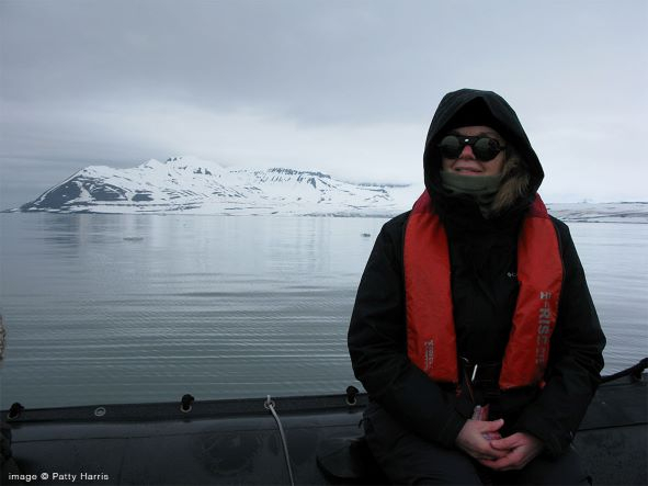 Woman bundled in winter coat and hood standing on boat with a glacier in the distance