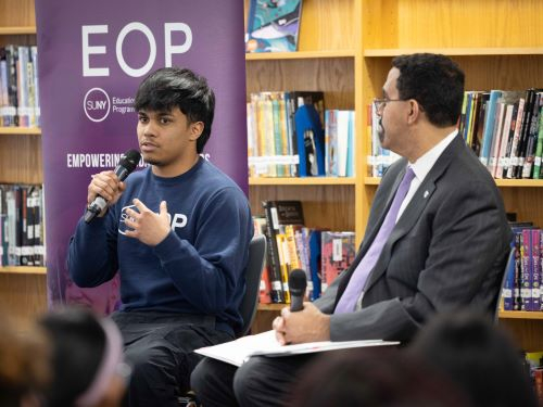 Hispanic young adult speaks into a microphone with EOP banner behind him