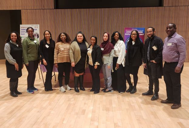 11 people of diverse races posing on stage for a group photo