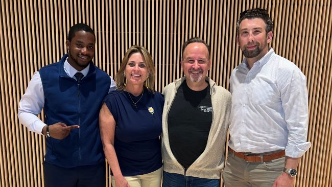 A young African American male students poses with event panelists, a woman and two other  men