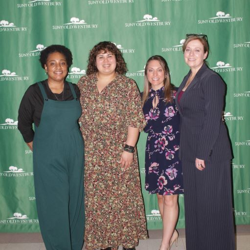 Four women pose before a green and white step-and-repeat banner
