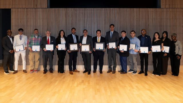 15 people in professional attire with 10 of them posing with award certificates