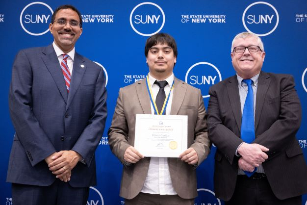 Young Hispanic male accepts award from an African American man and a white man