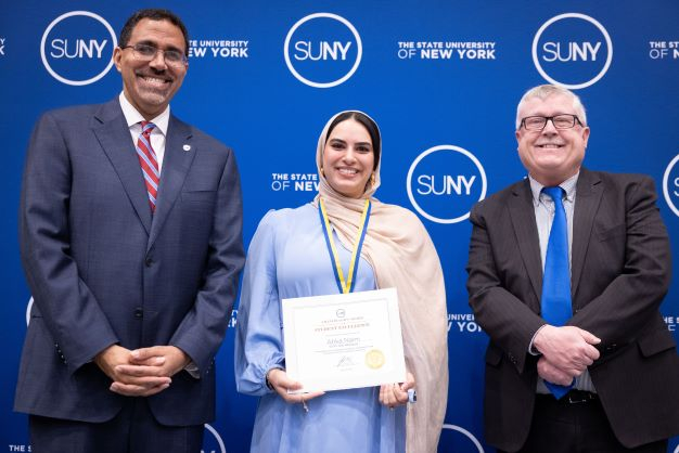 Young woman wearing habib accepts award from an African American man and a white man