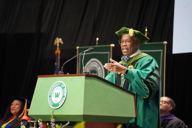 African American man in green regalia speaks from a podium