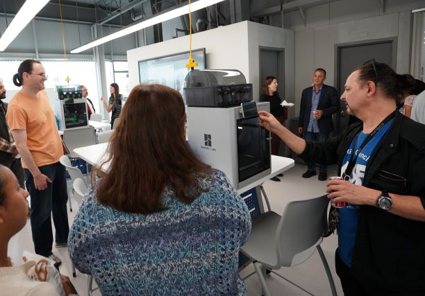 Students and faculty gather around a new 3D printer as it prints an item