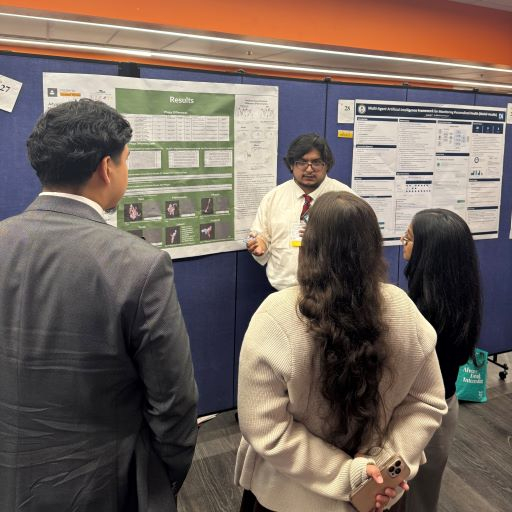 Young male in shirt and tie explains information from a poster hung on the wall to a small group of people