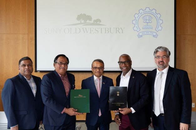 A group of five men from diverse backgrounds pose with two holding folders before a screen showing the logos of the Indian Institute of Technology Bombay and SUNY Old Westbury