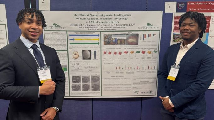 Two young African American males in professional attire pose before a scientific poster presentation