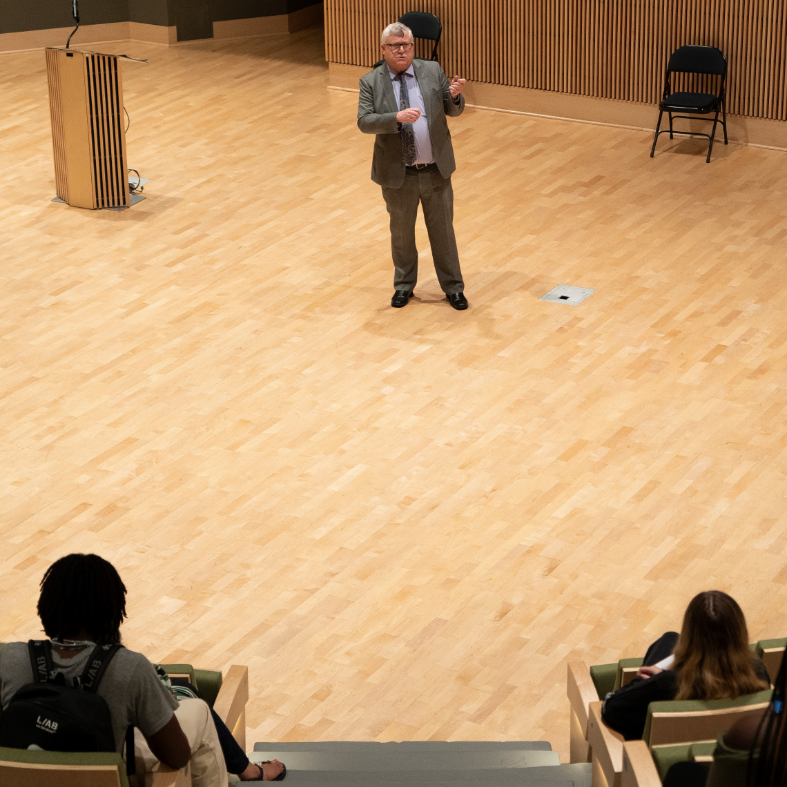 Older white man lectures to an audience of college-aged students