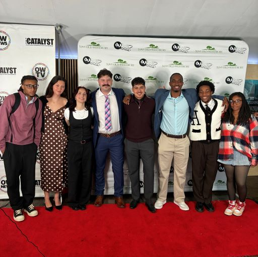 Seven young men and women posing on a red carpet before two step and repeat banners featuring student media logos