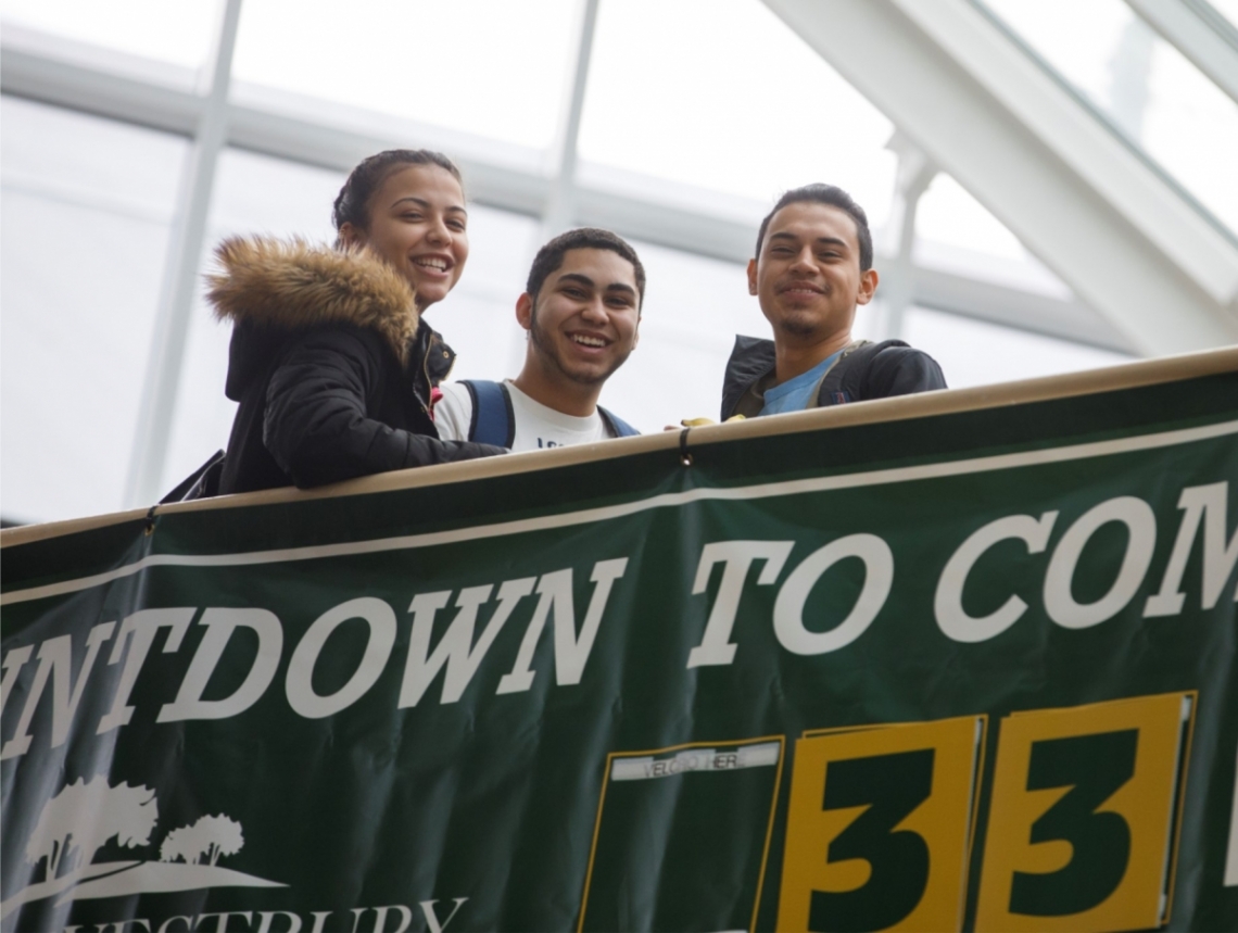 Three students smiling over count down to commencement banner