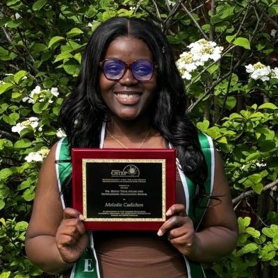 Smiling young black women with glasses holds an award plaque
