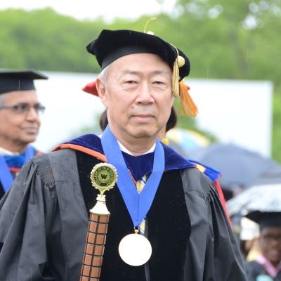 Older Asian American man dressed in regalia, wearing a medal and holding a ceremonial mace