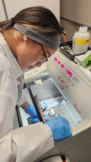 Hispanic woman in lab coat and rubber gloves manipulates samples in a laboratory setting