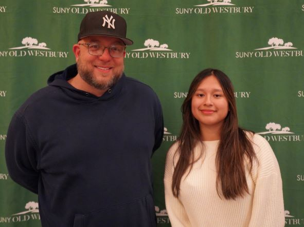 Man wearing a baseball cap stands with young woman before a green and white step-and-repeat banner