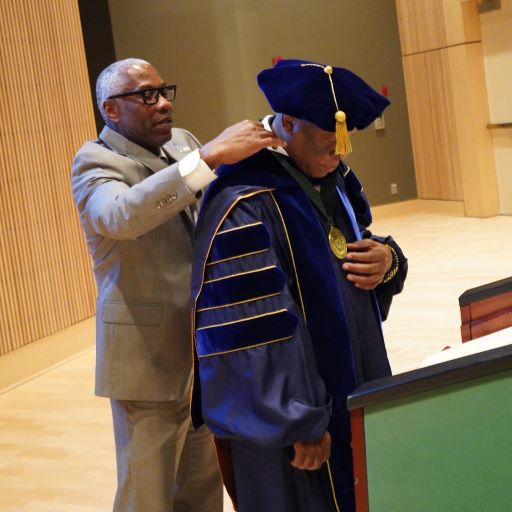 African American man in suit places a medal around the neck of an African American man in purple regalia