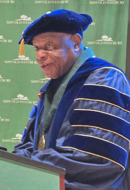 African American man in purple regalia speaks from a podium