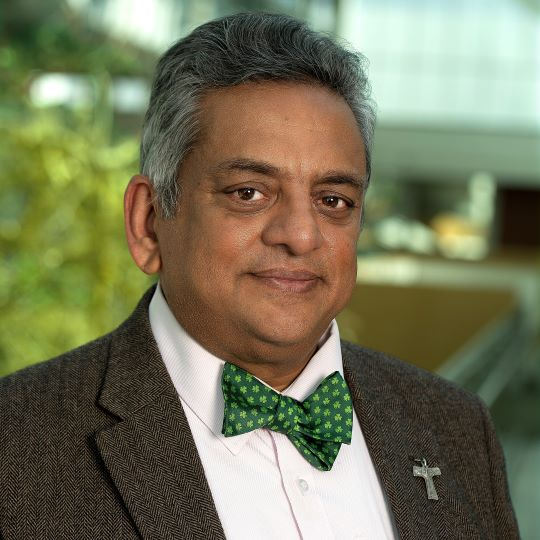 A man in a bow tie and green jacket smiling confidently.