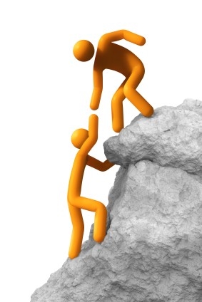 one person helping another person climb a rock