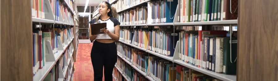 Female student walking among bookshelves