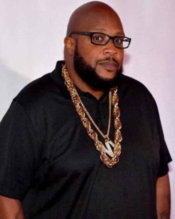 Bald African American man in black shirt wearing glasses and several gold necklaces