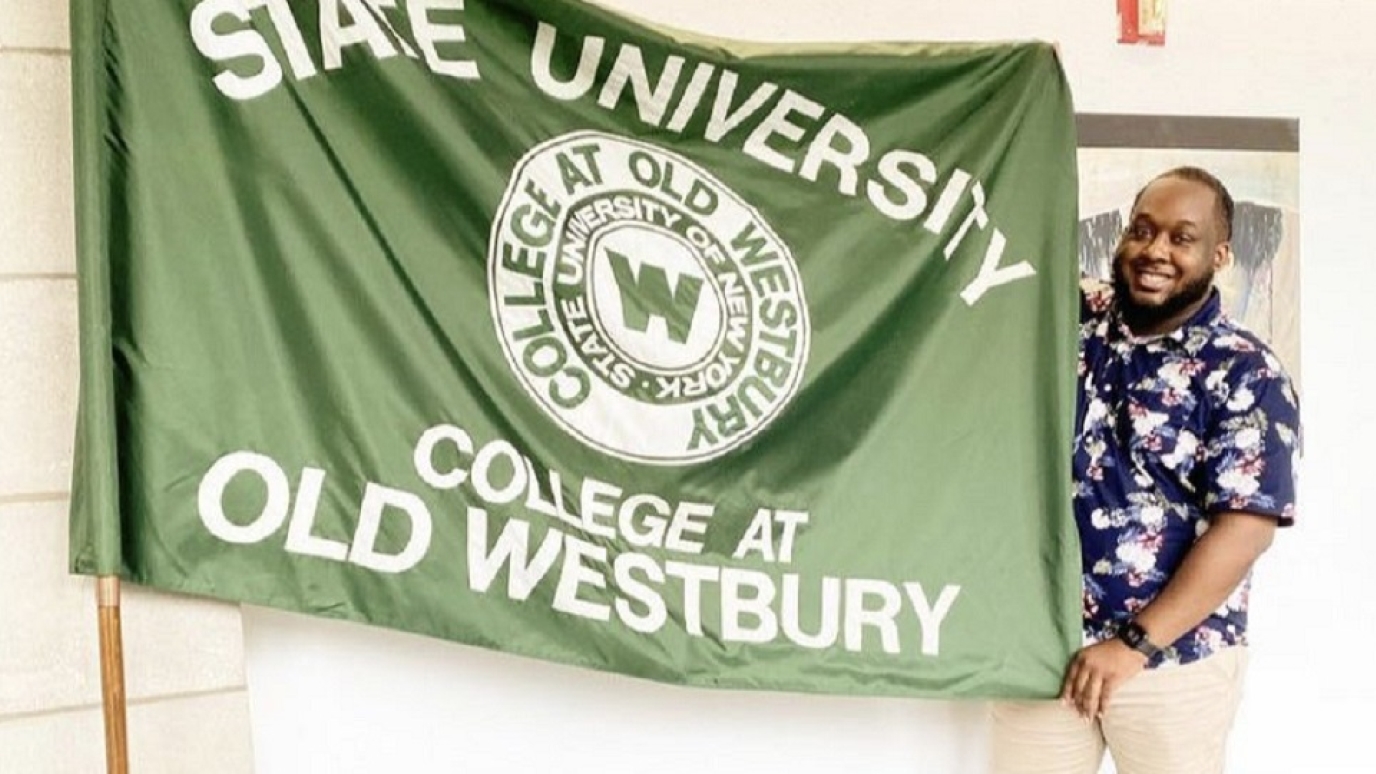 Kalief Metellus stands with the College flag that is on display in SUNY headquarters