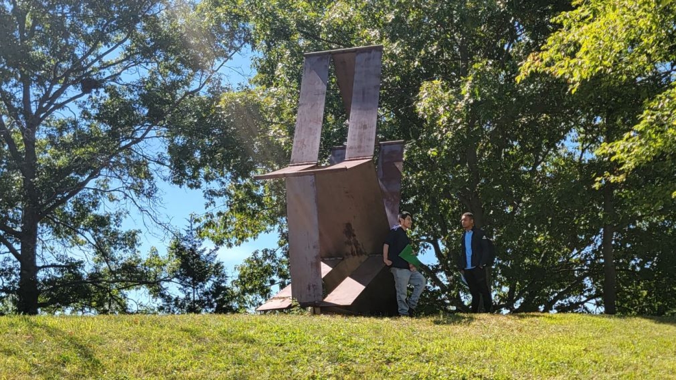 Two male students talk near a sculpture